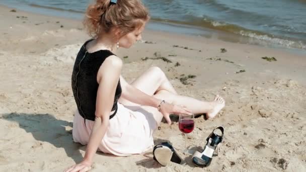 Νεαρή ξανθιά γυναίκα σε ένα όμορφο φόρεμα, απολαμβάνοντας ένα ποτήρι ροζέ κρασί στην παραλία κοντά στη θάλασσα, σούπερ αργή κίνηση — Αρχείο Βίντεο