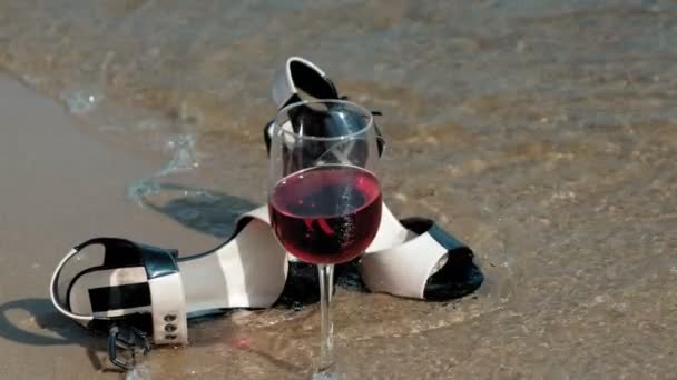 Zapatos se encuentran en la orilla del mar, una copa de vino se encuentra al lado — Vídeos de Stock