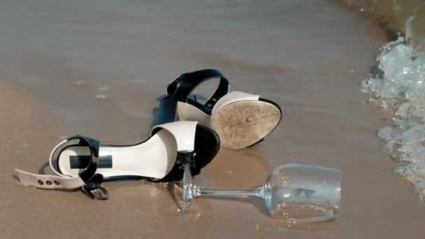 Zapatos se encuentran en la orilla del mar, una copa de vino se encuentra al lado — Vídeo de stock