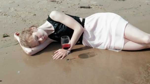 Femme ivre se couche sur la plage avec un verre de vin après une fête — Video