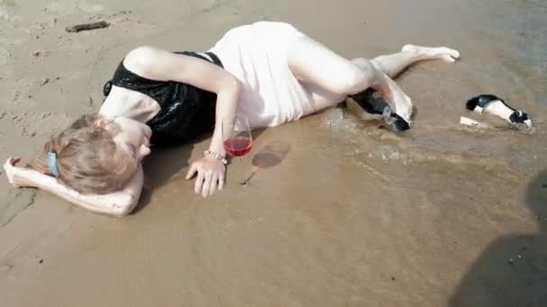 Dronken vrouw ligt aan het strand met een glas wijn na een feest — Stockvideo