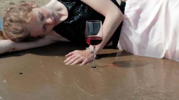 Betrunkene Frau liegt nach Party mit einem Glas Wein am Strand — Stockvideo