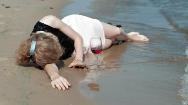 Dronken vrouw ligt aan het strand met een glas wijn na een feest — Stockvideo