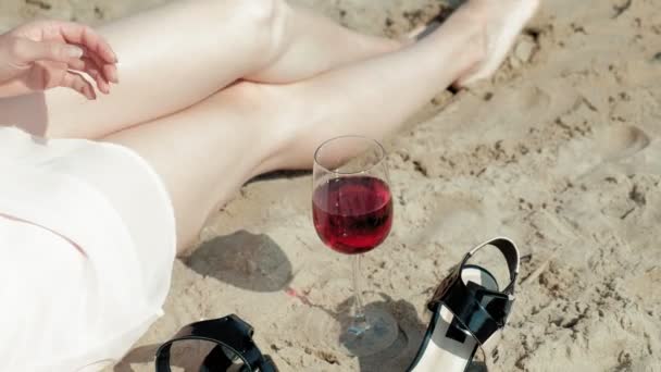 Jonge blonde vrouw in een mooie jurk, genieten van een glas roze wijn op het strand in de buurt van de zee, super slow motion — Stockvideo