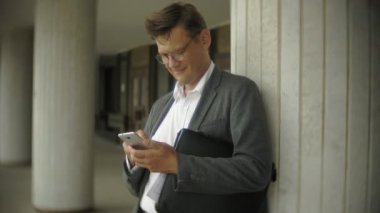 İş adamı merdivenlerden şehirde oturuyor. Bir takım elbise ve evrak çantası giyiyor. O belgeler üzerinden baktı ve smartphone üzerinde görüşmeler