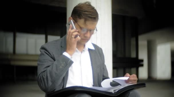 사업가 도시에 있는 계단에 앉아 있다. 그는 양복과 서류 가방을 착용. 그는 문서를 통해 외모와 스마트폰 이야기 — 비디오