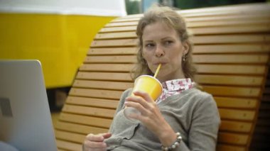 Milkshake ve dizüstü bilgisayar açık havada rahat bir yaratıcı banka olan kadın