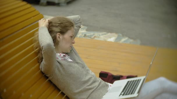 Ung kvinna med milkshake och bärbara utomhus på en bekväm kreativa bänk — Stockvideo