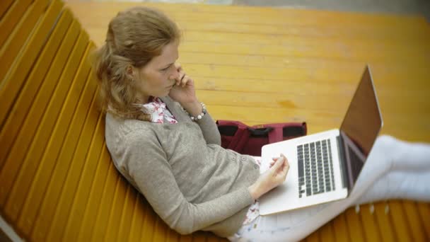 Молодая женщина с молочным коктейлем и ноутбуком на открытом воздухе на удобной креативной скамейке — стоковое видео