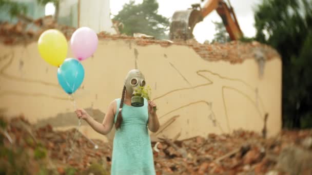 一个戴防毒面具的小女孩穿过废墟中的建筑, 手里拿着气球。 — 图库视频影像