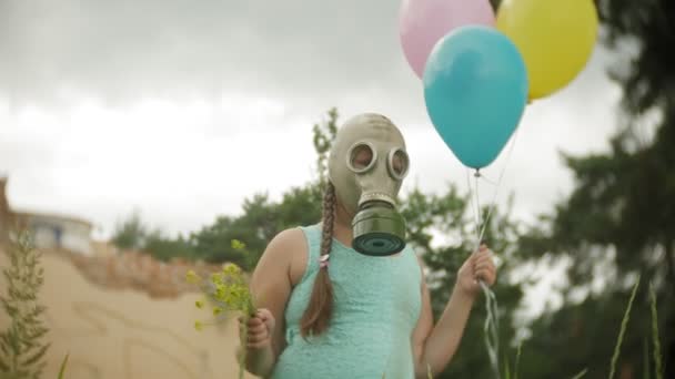 Una niña con una máscara de gas camina por los edificios arruinados con globos en la mano — Vídeos de Stock