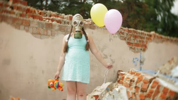 Una bambina con una maschera antigas sulle rovine di un edificio e aggrappata a una bambola e palloncini . — Video Stock