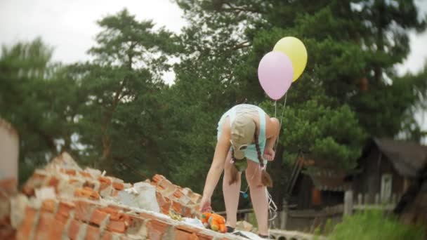 A little girl in a gas mask on the ruins of a building and holding on to a doll and balloons. — Stock Video