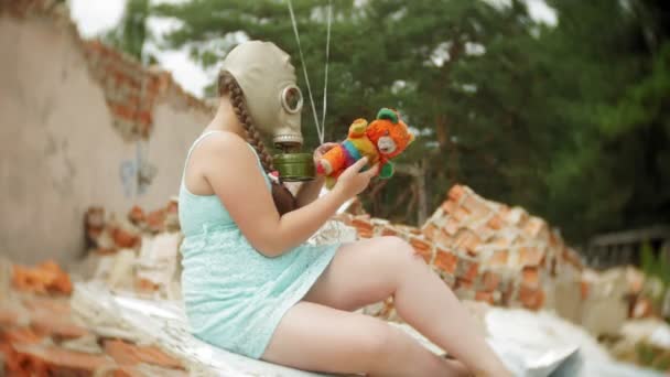 Una bambina con una maschera antigas sulle rovine di un edificio e aggrappata a una bambola e palloncini . — Video Stock