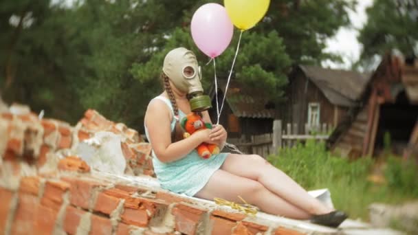 一个在建筑物废墟上防毒面具的小女孩 手持一个洋娃娃和气球 — 图库视频影像
