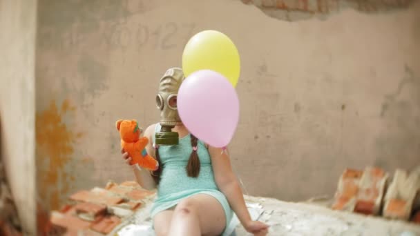 A little girl in a gas mask on the ruins of a building and holding on to a doll and balloons. — Stock Video