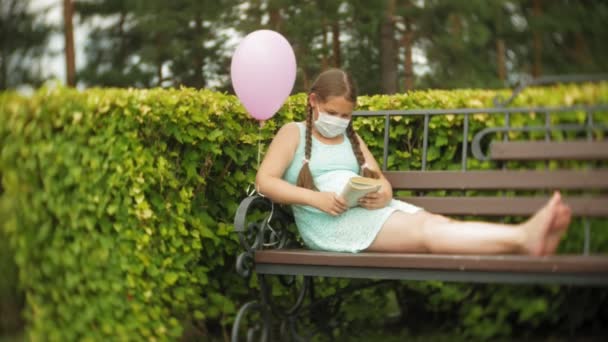 Cute girl in a respirator reading a book in the park on a bench — Stock Video