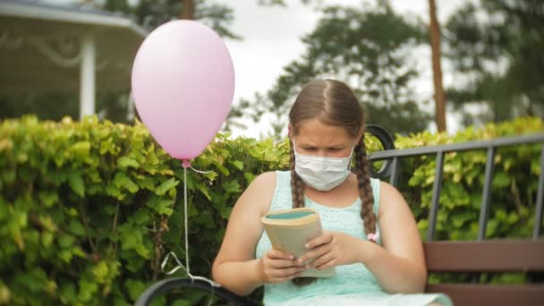 Ładna dziewczyna w respirator z książką w parku na ławce — Wideo stockowe