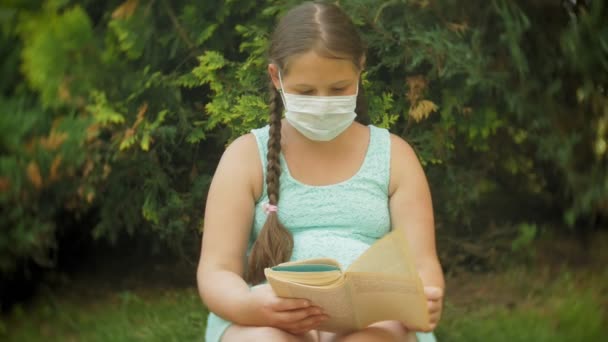 Ragazza carina in un respiratore che legge un libro nel parco su una panchina — Video Stock