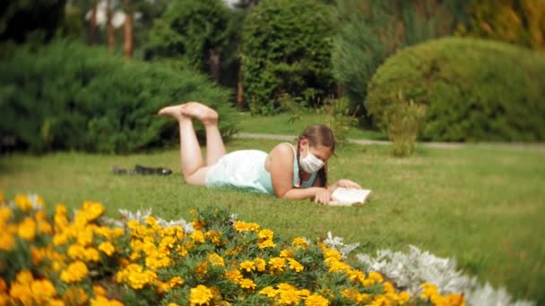 Menina bonito em um respirador lendo um livro no parque — Vídeo de Stock