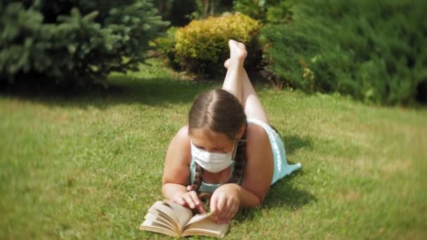 Schattig meisje in een gasmasker lezen van een boek in het park — Stockvideo