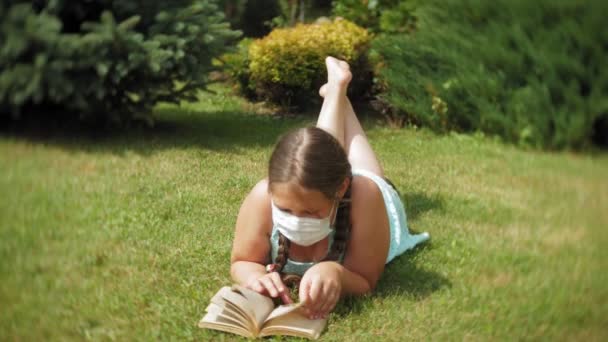 Linda chica en un respirador leyendo un libro en el parque — Vídeos de Stock