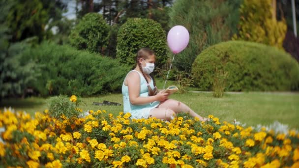 Schattig meisje in een gasmasker lezen van een boek in het park — Stockvideo