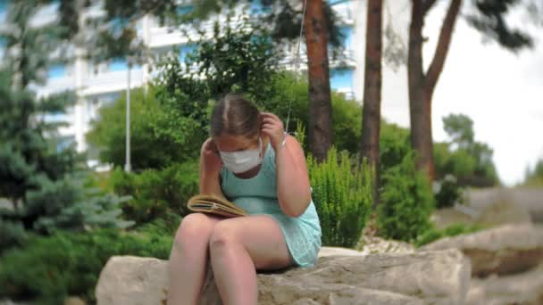 Linda chica en un respirador leyendo un libro en el parque — Vídeos de Stock