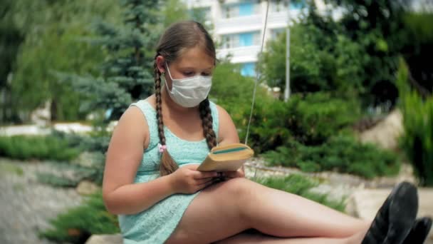 Menina bonito em um respirador lendo um livro no parque — Vídeo de Stock