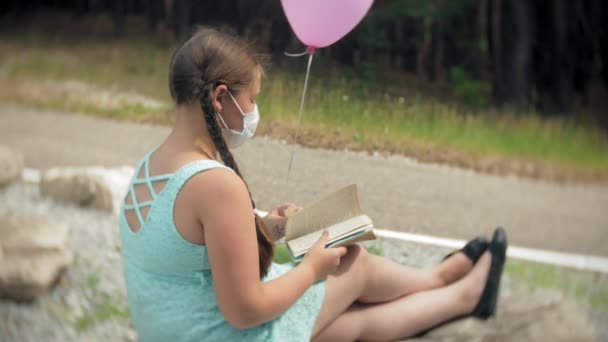 Χαριτωμένο κορίτσι σε μια αναπνευστική συσκευή διαβάζοντας ένα βιβλίο στο πάρκο — Αρχείο Βίντεο