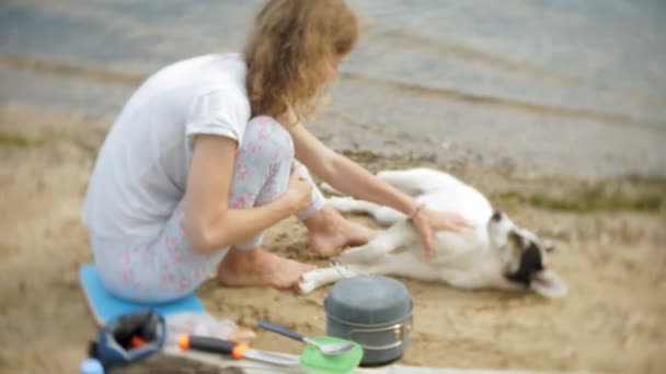 Wanita memasak makanan di Bowler saat berkemah dengan tenda di belakangnya. anjing berjalan di samping — Stok Video