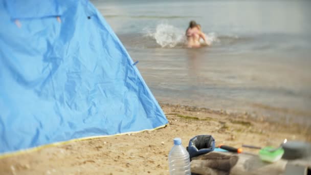 Niños bañan un hervidor de agua en un camping con una tienda de campaña en el fondo . — Vídeo de stock