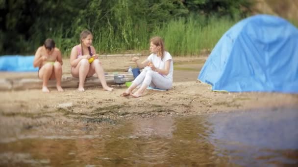 Una mujer y sus hijos están comiendo una comida cerca de la tetera en un campamento con una tienda de campaña en el fondo . — Vídeo de stock