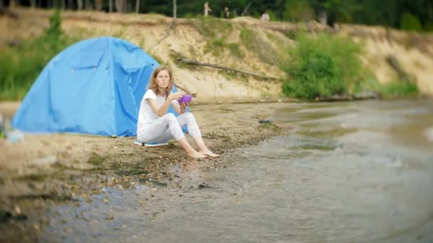 Bir kadın bir kazana arka planda bir çadır ile bir kamp çevresinde yiyor. — Stok video