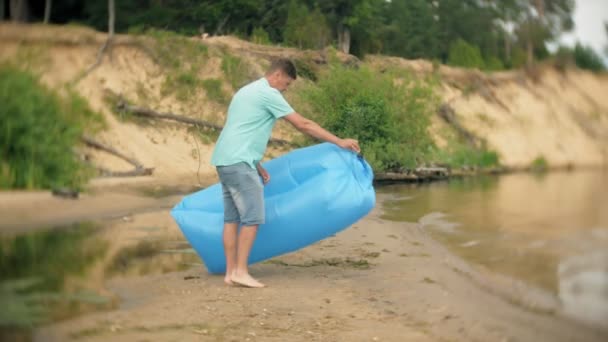 En man blåsa på en uppblåsbar madrass vid havet. — Stockvideo
