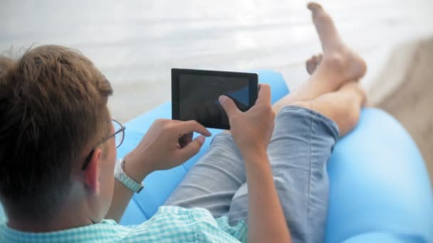 Egy ember nyugszik egy felfújható matrac, a tenger mellett. Ő használ egy tabletta — Stock videók