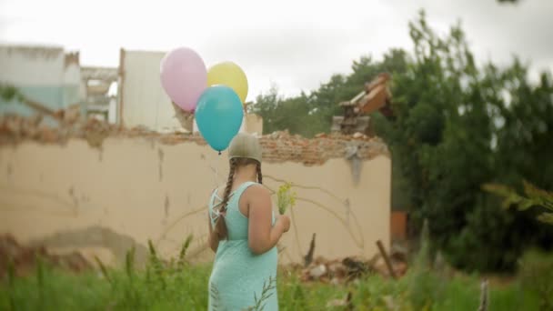 Een klein meisje in een gasmasker wandelingen door de verwoeste gebouwen met ballonnen in haar hand — Stockvideo