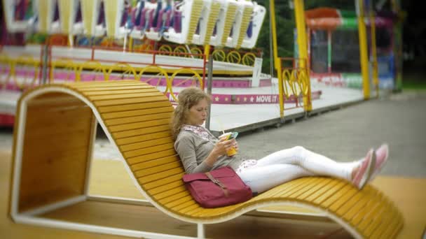 Молода жінка з молочним коктейлем і мобільним телефоном на відкритому повітрі на зручній творчій лавці — стокове відео
