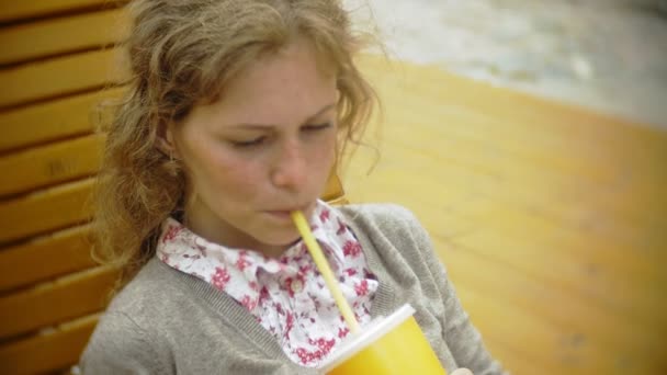Молода жінка з молочним коктейлем і мобільним телефоном на відкритому повітрі на зручній творчій лавці — стокове відео