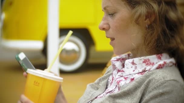 Giovane donna con frullato e cellulare all'aperto su una comoda panchina creativa — Video Stock