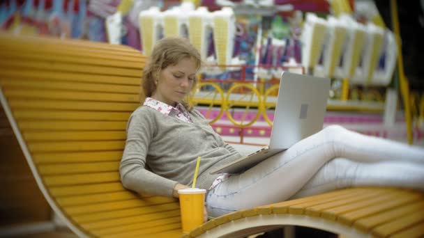 Jonge vrouw met milkshake en laptop buiten op een comfortabele creatieve Bank — Stockvideo