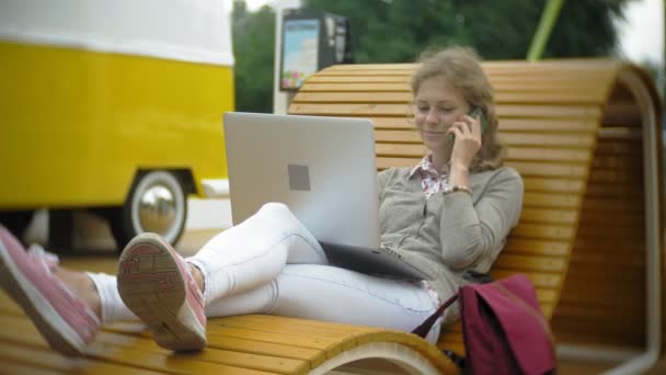 Young woman with milkshake and laptop outdoors on a comfortable creative bench — Stock Video