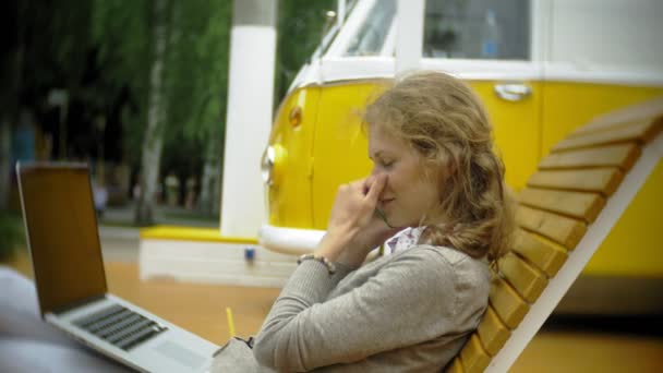 Jeune femme avec milkshake et ordinateur portable à l'extérieur sur un banc créatif confortable — Video