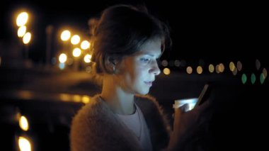 Şehir merkezinde ise cep telefonuna gece genç kadın mesaj. Mutlu kadın manifatura ile şehir içinde smartphone.