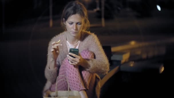 Jovem mulher comendo batatas fritas na noite ao ar livre pela luz das lanternas — Vídeo de Stock