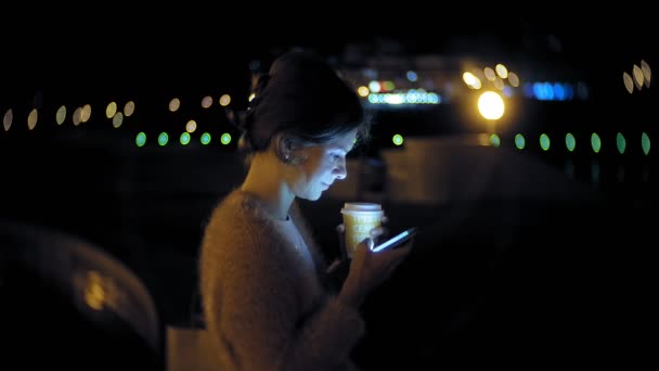 Jovem mensagem de texto mulher no telefone celular, enquanto o centro da cidade à noite. mensagens de texto feminino feliz com smartphone na cidade . — Vídeo de Stock