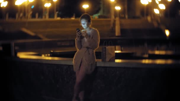 Young woman text messaging on mobile phone while downtown at night. Happy female texting with smartphone in the city. — Stock Video