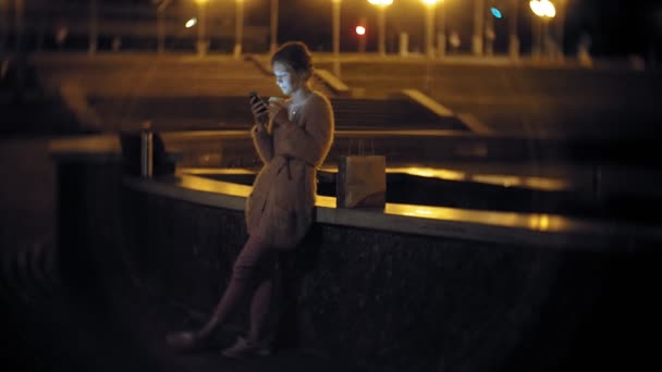 Jovem mensagem de texto mulher no telefone celular, enquanto o centro da cidade à noite. mensagens de texto feminino feliz com smartphone na cidade . — Vídeo de Stock