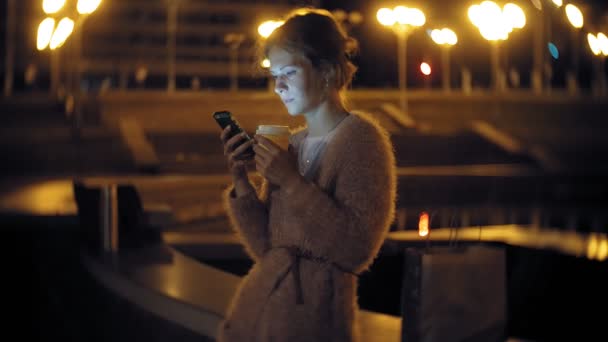 Jovem mensagem de texto mulher no telefone celular, enquanto o centro da cidade à noite. mensagens de texto feminino feliz com smartphone na cidade . — Vídeo de Stock