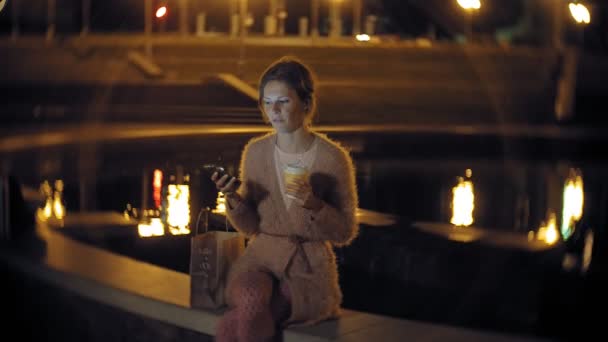 Tânăra femeie trimite mesaje text pe telefonul mobil în timp ce se află în centru noaptea. Mesaje de sex feminin fericite cu smartphone-uri în oraș . — Videoclip de stoc